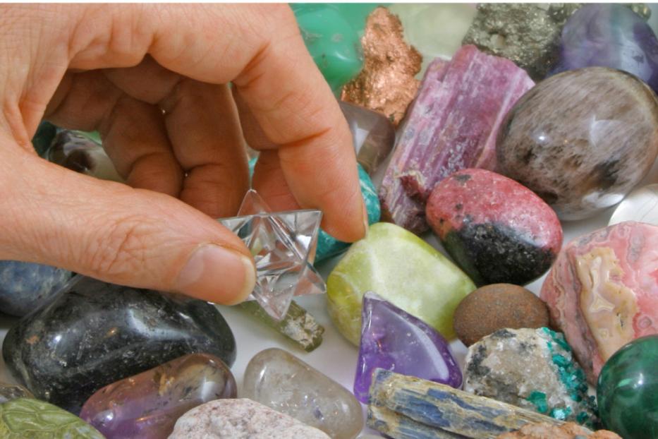 Eine Hand hält einen klaren Merkabah-Stern über einer Sammlung von Edelsteinen.