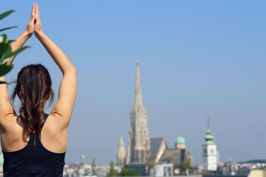 Eine Frau macht Yoga vor der Skyline von Wien mit dem Stephansdom.