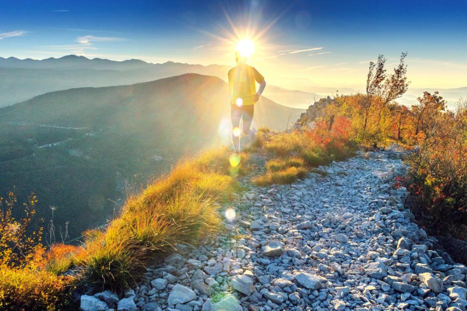 Ein Läufer auf einem steinigen Pfad in den Bergen, mit der Sonne im Rücken.