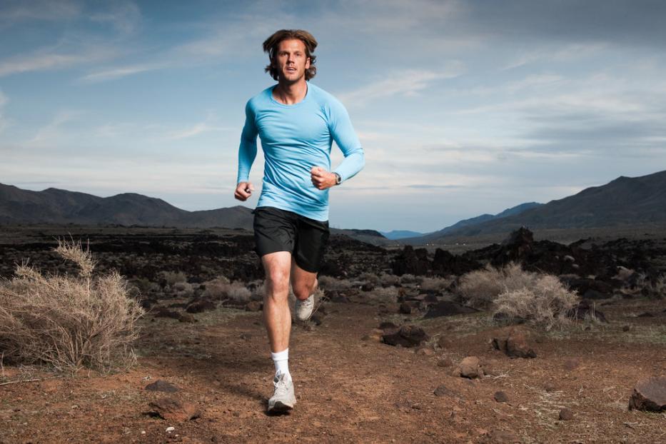 Ein Mann joggt in Sportkleidung durch eine karge Landschaft mit Bergen im Hintergrund.