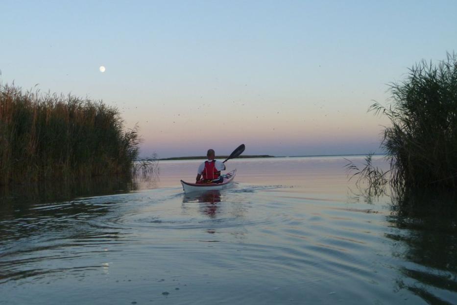 Ein Mann paddelt bei Sonnenuntergang in einem Kajak auf einem ruhigen See.