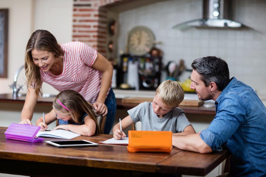 Vater, Mutter und ihre beiden Schulkinder beim Hausaufgaben machen