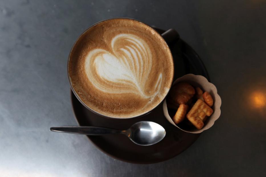 Ein Cappuccino mit Herzmuster im Milchschaum, serviert mit einer kleinen Portion Gebäck.
