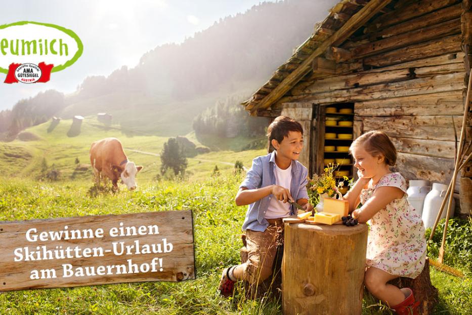 Ein Junge und ein Mädchen sitzen vor einer Hütte und schneiden Käse, im Hintergrund eine Kuh auf einer Wiese.