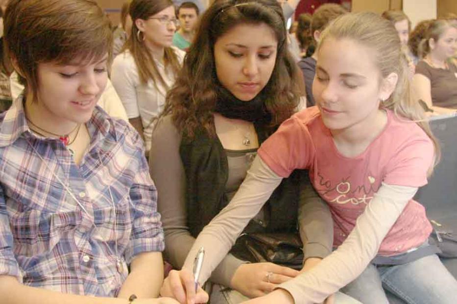 Drei junge Frauen sitzen zusammen und schreiben oder zeichnen etwas.