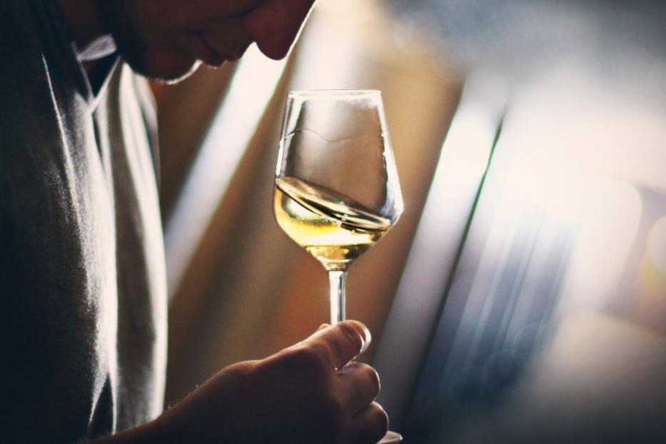 Junger Mann bei einer Weinverkostung mit einem Glas Wein in der Hand.