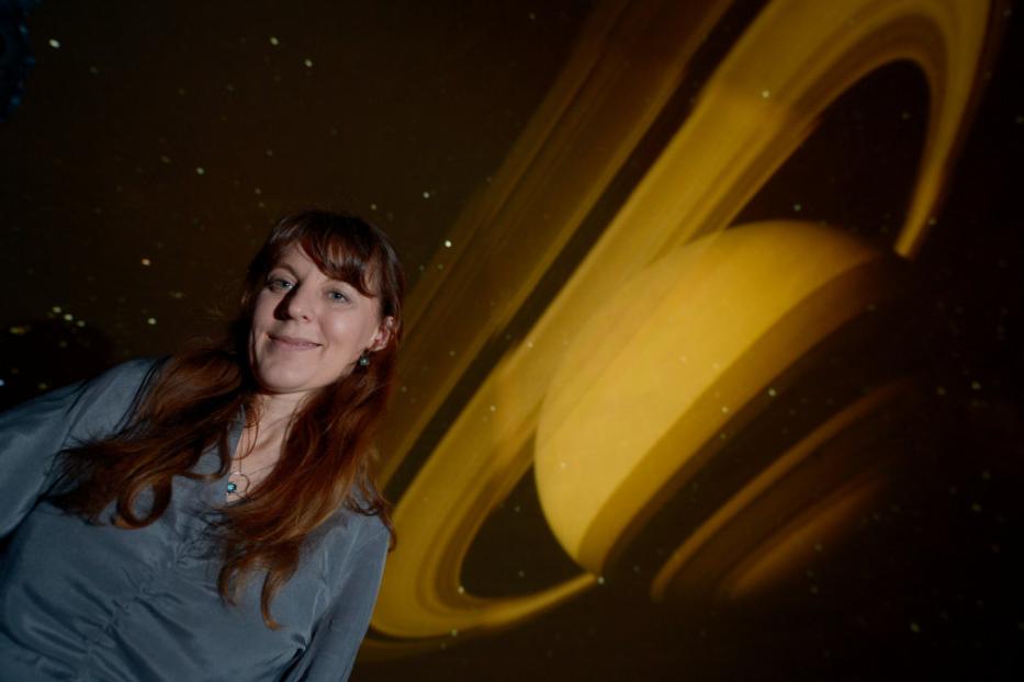 Eine Frau steht vor einer Projektion des Planeten Saturn.