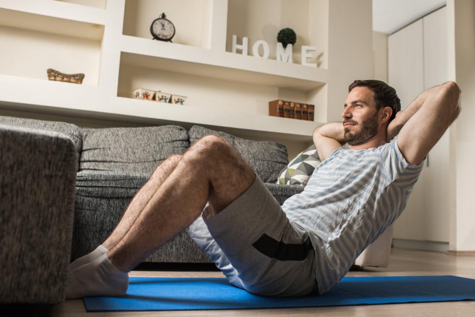 Ein Mann macht Sit-ups auf einer blauen Matte im Wohnzimmer.