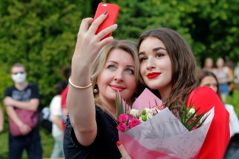 Zwei Frauen machen ein Selfie mit einem roten Smartphone, eine hält einen Blumenstrauß.