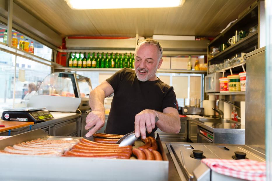 Ein Mann brät Würste in einem Imbisswagen.