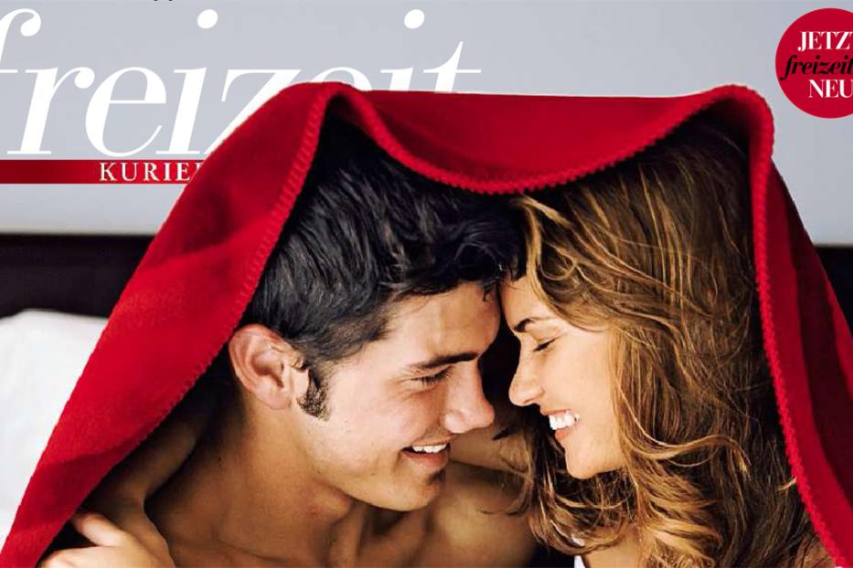 Ein lächelndes Paar kuschelt unter einer roten Decke.