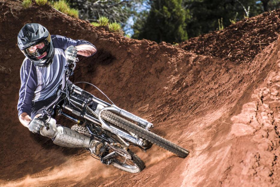 Ein Mountainbiker fährt eine steile, rote Sandpiste hinunter.