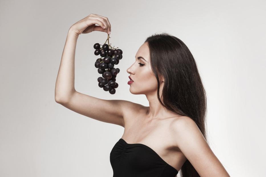 Eine Frau im schwarzen Kleid hält eine Traube hoch.