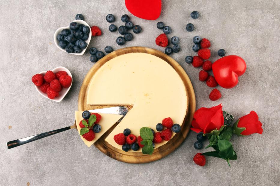 Ein Käsekuchen mit Beeren und einer Rose auf einem Holzteller.