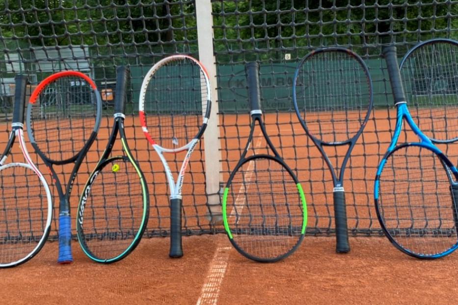 Mehrere Tennisschläger stehen an einem Tennisnetz auf einem Sandplatz.