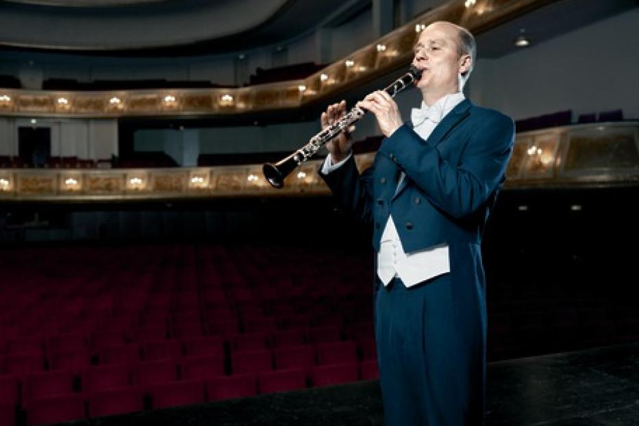 Ein Mann im Frack spielt Klarinette auf einer Bühne.