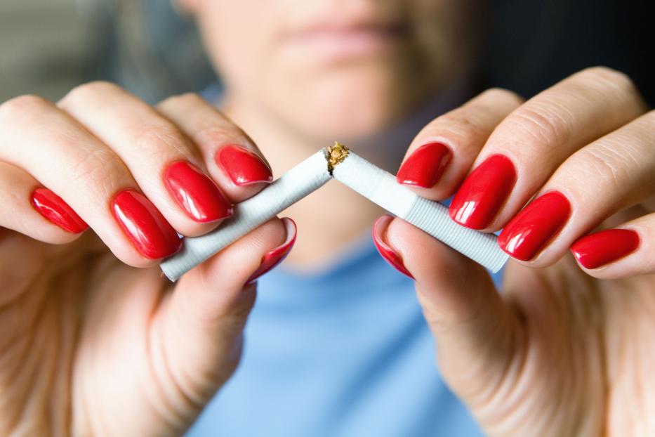 A girl with a beautiful manicure breaks a cigarette.