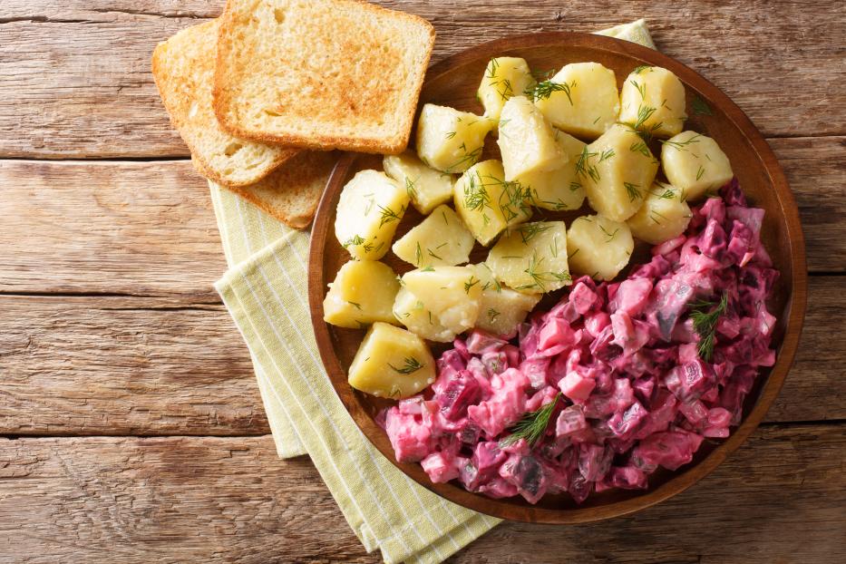 Tasty herring salad with vegetables and a side dish of boiled potatoes close-up in a plate. Horizontal top view