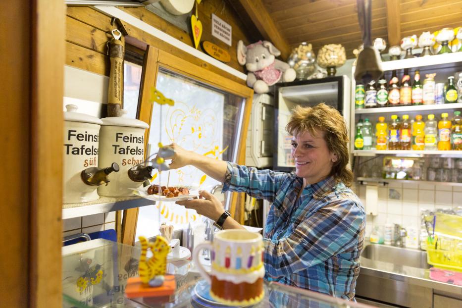 Eine Frau in einem Imbiss bereitet eine Portion Currywurst zu.