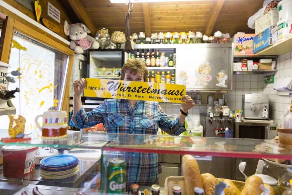 Eine Frau hält ein Schild mit der Aufschrift „I fahr zur Würstelmausi“ in Wien.