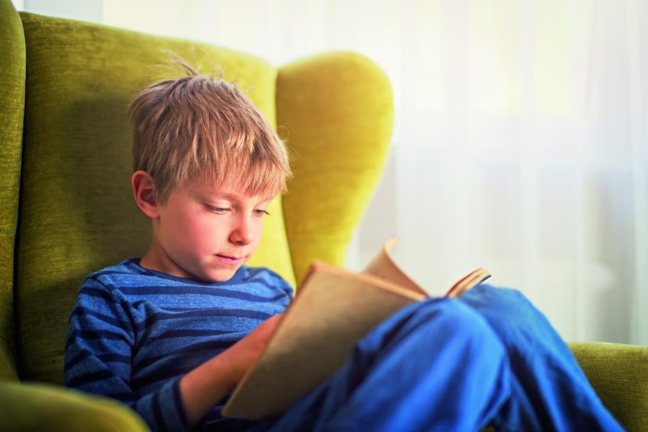 Little boy reading a book in green armchair