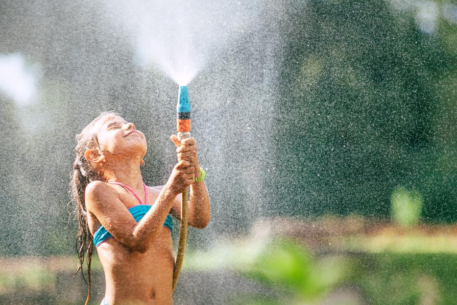 Cute little girl pours herself from the hose, makes a rain. Hot summer day pleasure