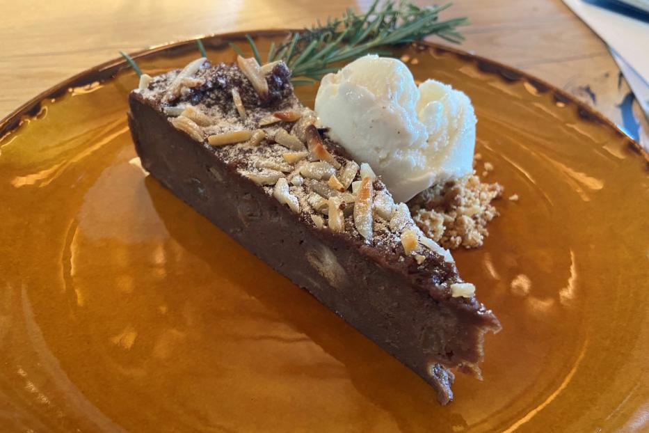 Ein Stück Schokoladenkuchen mit Mandeln und einer Kugel Eis auf einem Teller.