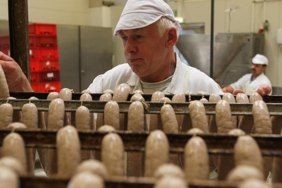 Ein Metzger hängt Würste in einer Wurstfabrik auf Stangen.