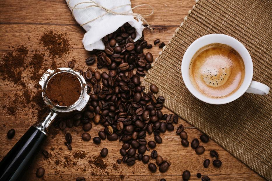 Kaffeetasse mit Siebträger und ganzen Bohnen daneben