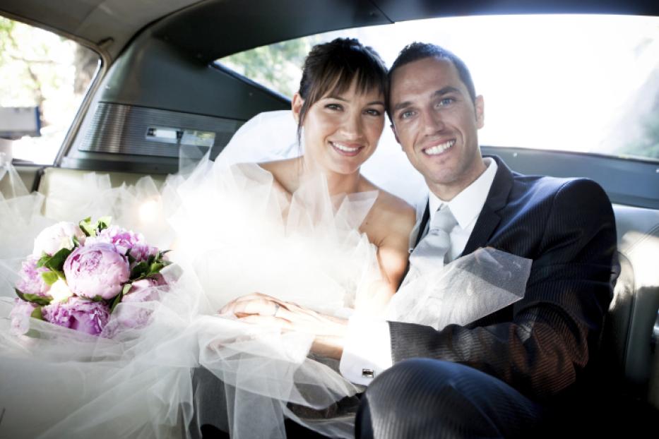 Ein Brautpaar sitzt mit einem Blumenstrauß im Fond eines Autos.