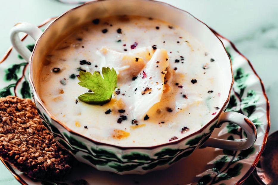 Eine Tasse cremige Suppe mit einem Keks und einem Glas Wasser auf einem Marmortisch.
