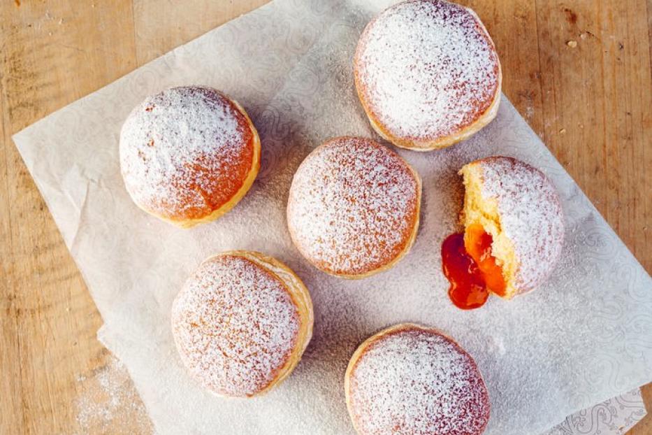 Sechs mit Puderzucker bestäubte Krapfen liegen auf einem Stück Papier.