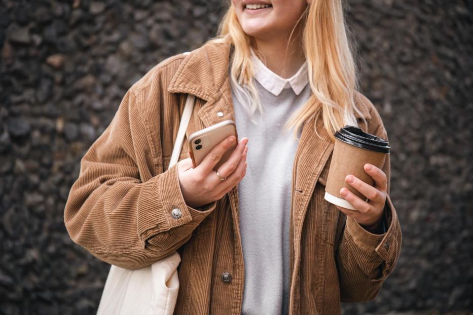 Nahaufnahme, eine Tasse Kaffee und ein Smartphone in weiblichen Händen in der Stadt