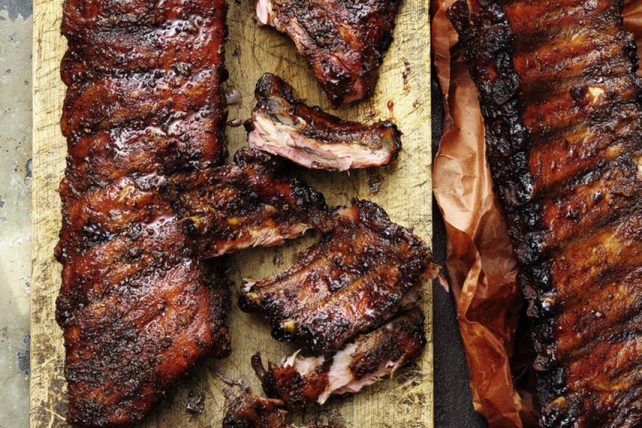 Spareribs, teilweise geschnitten, liegen auf einem Holzbrett und braunem Papier.