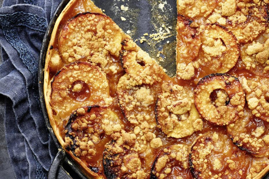 Ein Apfelkuchen mit Streuseln in einer schwarzen Pfanne, ein Stück fehlt.