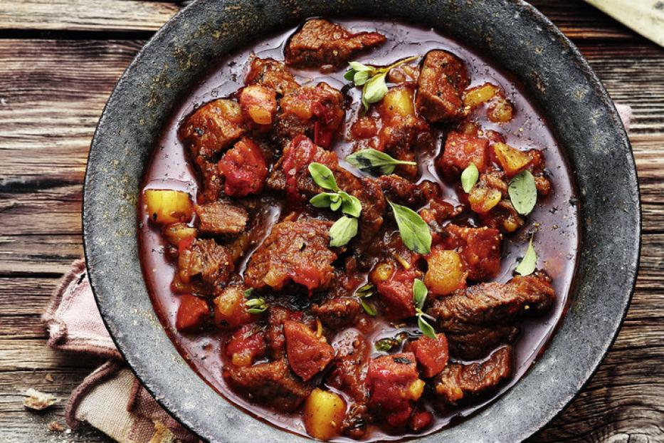 Ein Teller mit herzhaftem Gulasch, garniert mit frischen Kräutern, steht auf einem Holztisch.