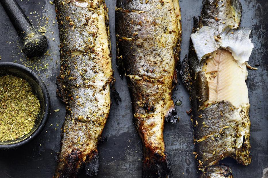 Gegrillte Forellen auf einem dunklen Teller mit Gewürzen und einem Teebeutel.