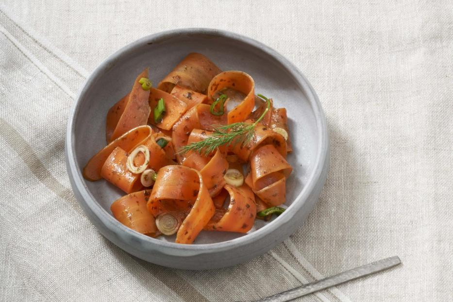 Ein grauer Teller mit Karottensalat und einer Gabel auf einem Tisch.