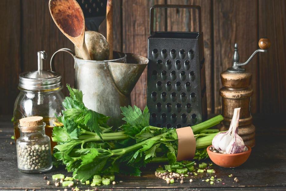 Rustic cooking set with vintage kitchen utensils and celery bunch on dark table at wooden background. - Stock-Fotografie