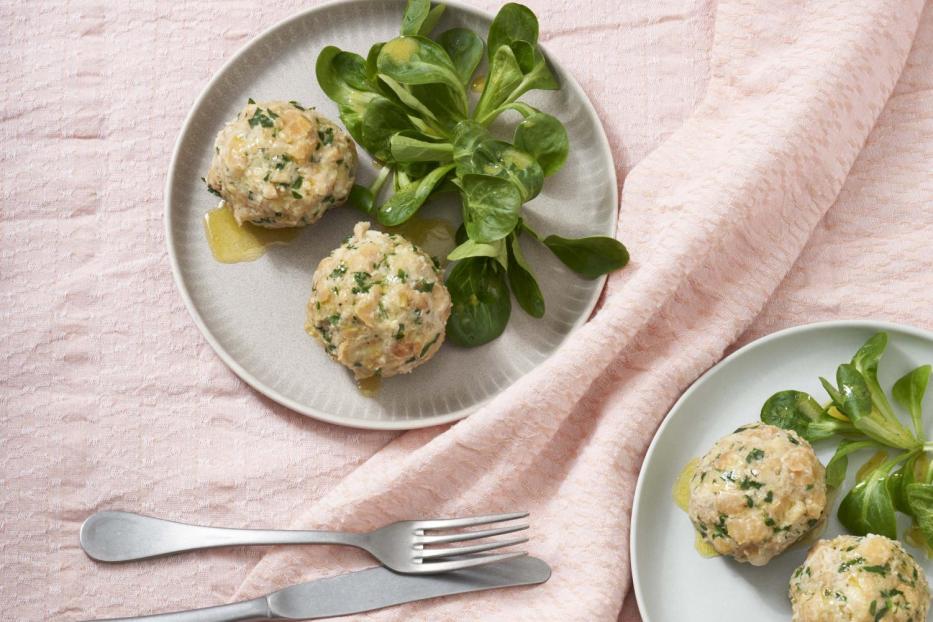 Zwei Teller mit Serviettenknödeln und Feldsalat auf einem rosa Tuch.
