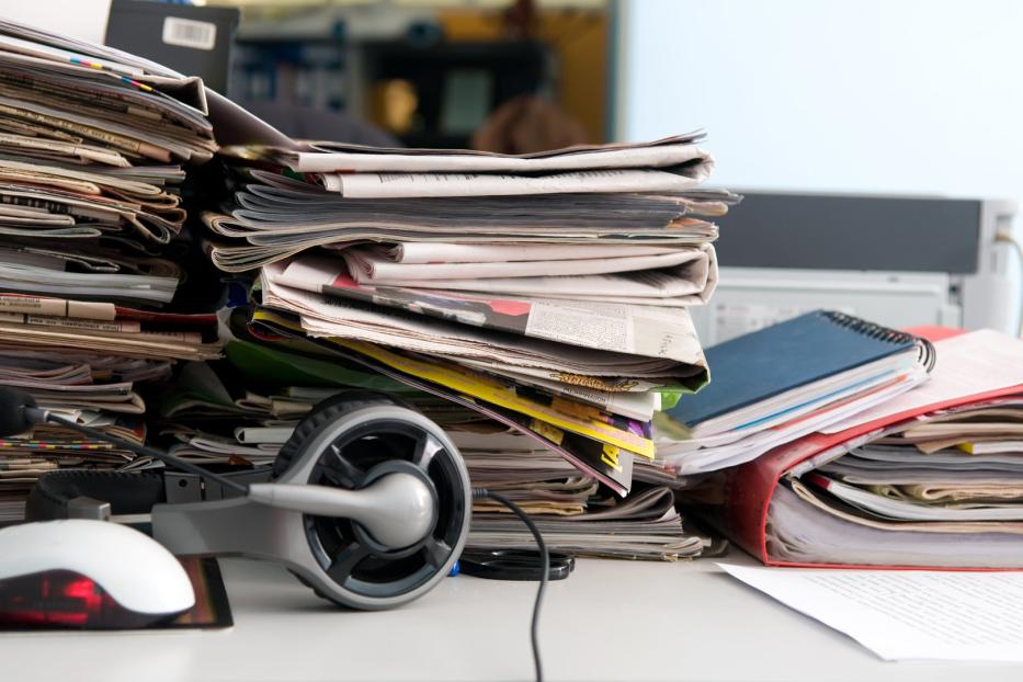 Ein Schreibtisch ist mit Papierstapeln, einem Headset und einer Maus bedeckt.