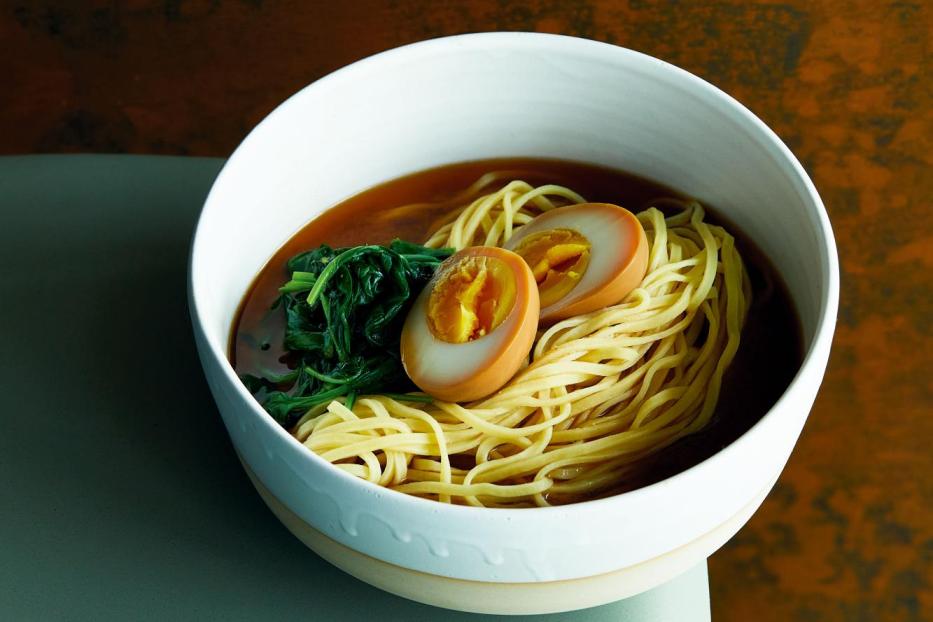 Eine Schüssel Ramen mit Nudeln, Ei und Gemüse steht auf einem Tisch.