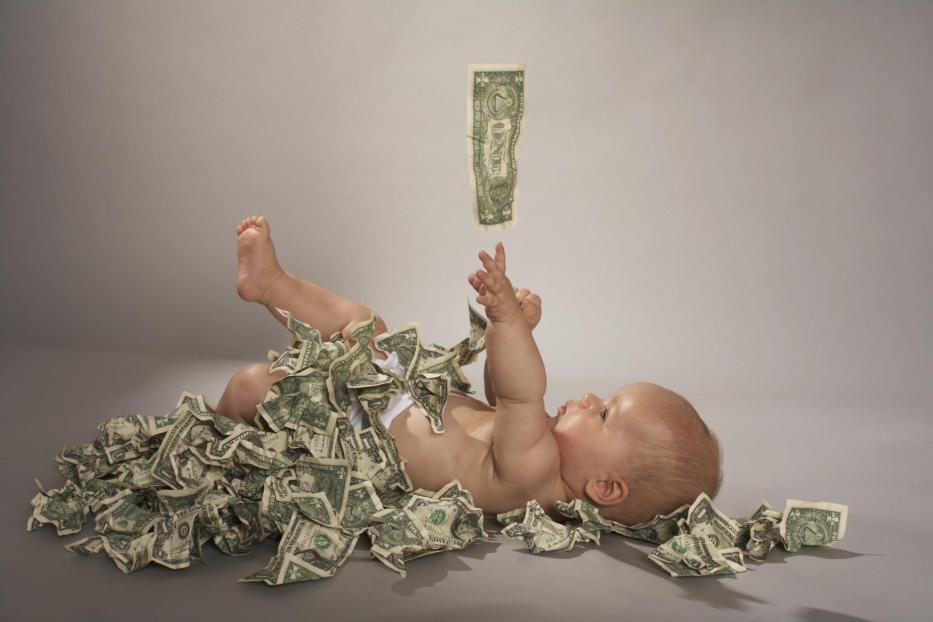 Baby girl (5 months) lying down covered with us dollar bills falling from above - Stock-Fotografie