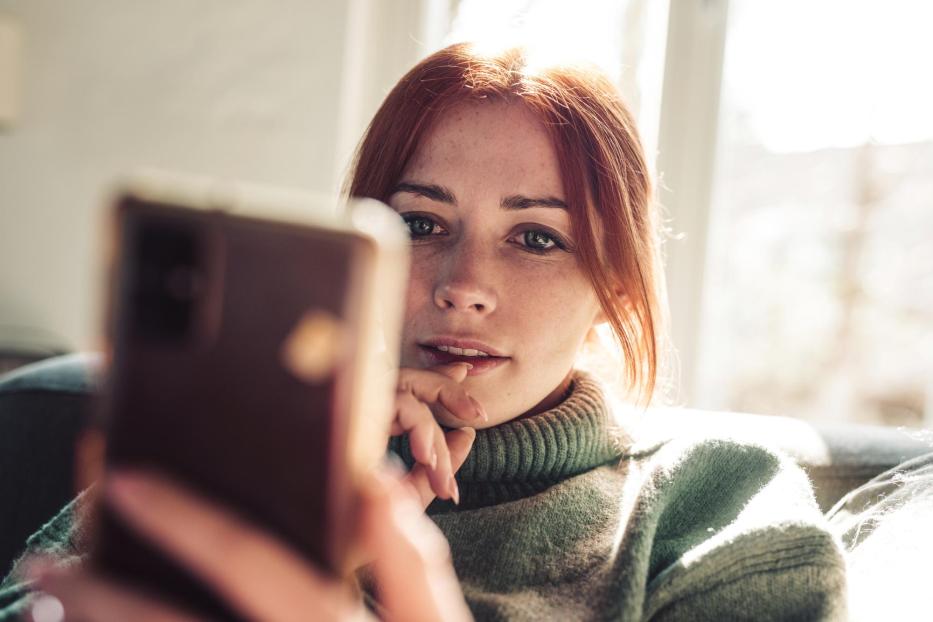 Woman with red hair looking on screen of her mobile phone. - Stock-Fotografie