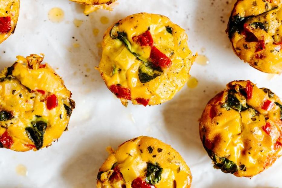 Mehrere Eier-Muffins mit Gemüse liegen auf einem weißen Untergrund.