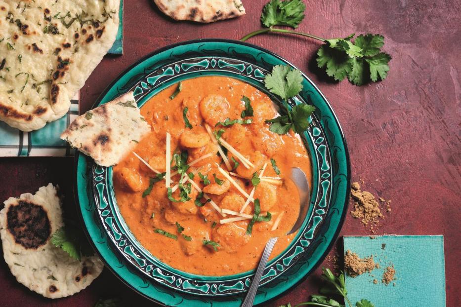 Ein Teller mit Garnelen-Curry und Naan-Brot auf einem roten Untergrund.