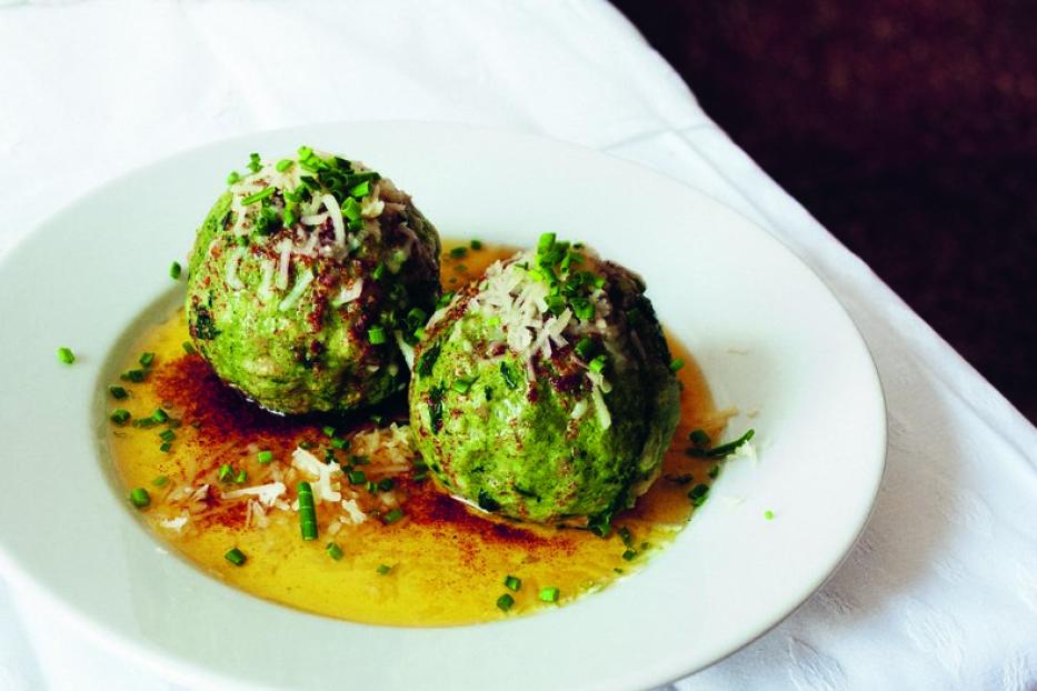 Zwei Spinatknödel liegen auf einem Teller mit zerlassener Butter und Parmesanraspeln.