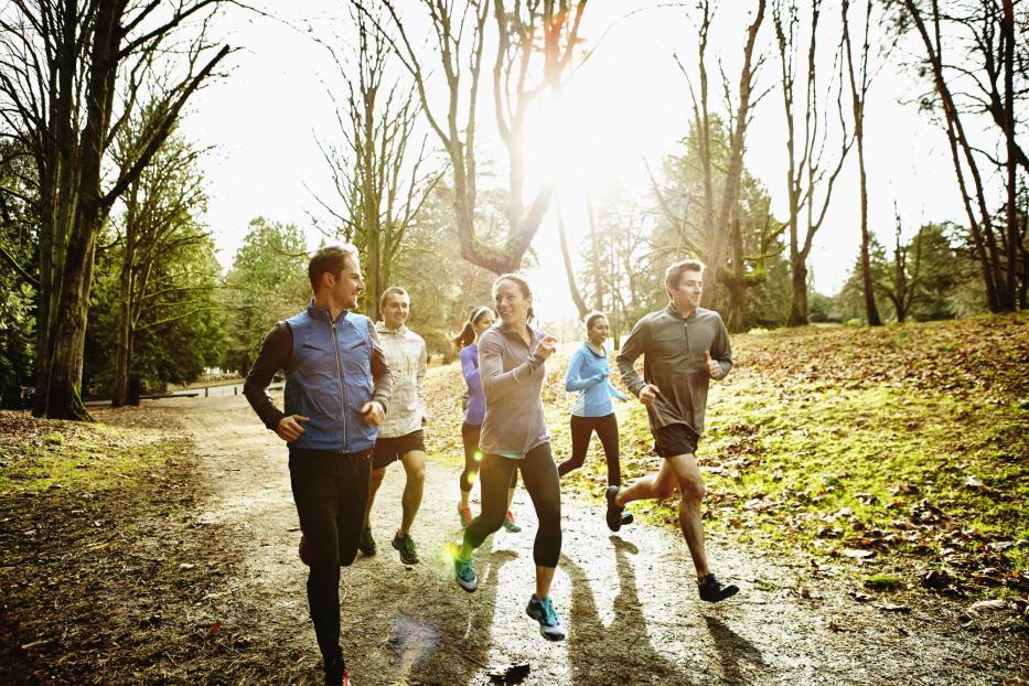 Smiling friends running together in park - Stock-Fotografie