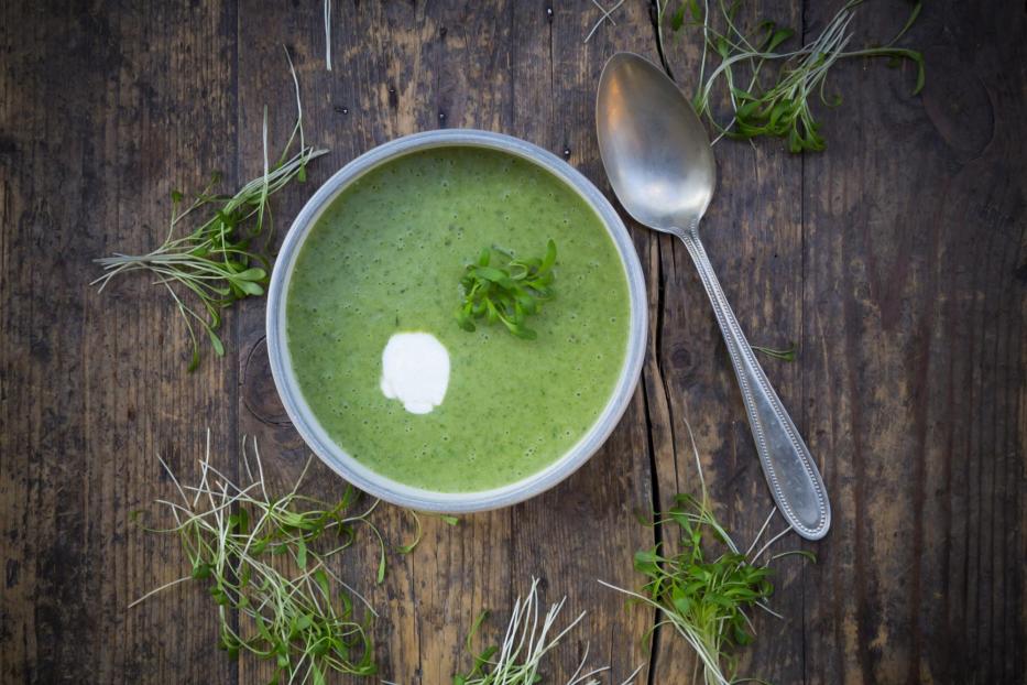 Eine Schüssel Kressesuppe mit einem Klecks Sahne auf einem dunklen Holztisch.