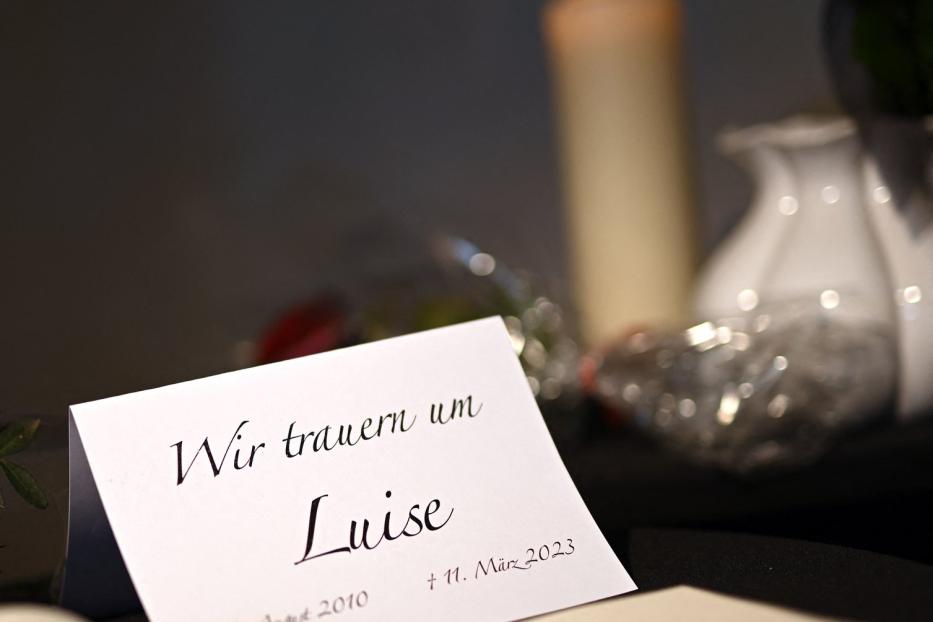 Eine Trauerkarte für Luise mit dem Datum 11. März 2023 liegt neben einer Kerze.